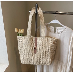 Detail of woven straw tote bag with brown leather strap and metal buckle accent