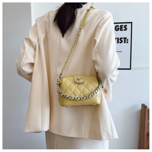 Detail of light yellow quilted crossbody bag with silver clasp and chain strap on model