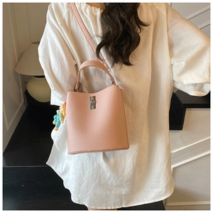 Detail of pink bucket bag with lychee texture and cute doll pendant on white shirt
