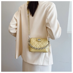 Detail of light yellow quilted crossbody bag with silver chain and turn-lock on a model