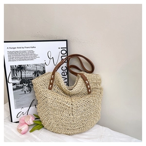 Detailed shot of beige woven straw tote with brown leather handles and white cross-stitching