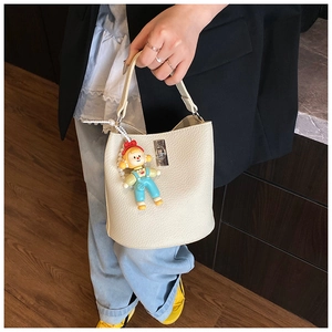 Detail of cream bucket bag with lychee texture, metal lock, and cartoon doll pendant