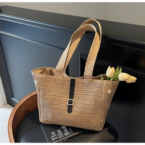 Detail of woven straw tote bag with black decorative strap and metal buckle on chair