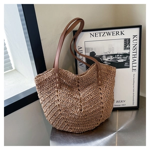 Detail of herringbone woven straw tote bag with brown leather strap against minimalist art