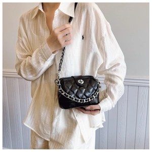 Model wearing a black quilted crossbody bag with silver chain strap and metal lock