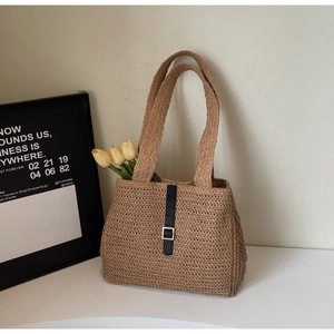 Detail of a brown woven straw tote bag with black vertical strap and silver buckle accent