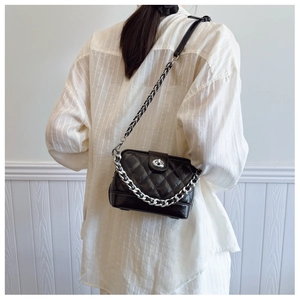 Detail of black quilted crossbody bag featuring silver chain and metal turn-lock closure
