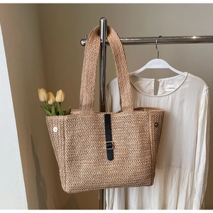 Detailed close-up of woven straw tote bag with black leather strap and buckle closure