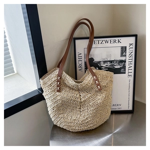 Detail of V-shaped woven straw tote bag with brown leather handles and decorative stitching
