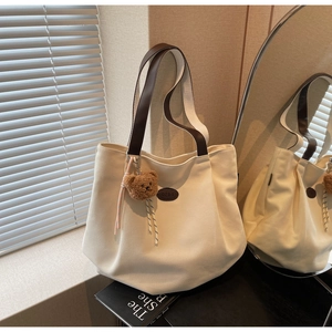 Détail du sac cabas en toile blanc cassé avec anses en cuir marron et charm ours en peluche