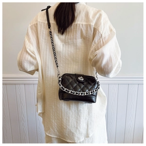 Rear view of model wearing a black quilted crossbody bag with silver chain strap