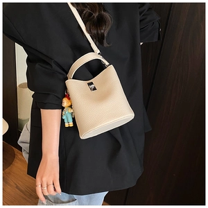 Detail of off-white bucket bag with lychee texture, silver buckle, and cute doll charm