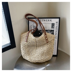 Detail of beige straw tote with V-pattern weave and brown leather straps on metal table