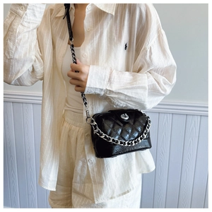Detail of a black quilted crossbody bag featuring a silver chain and twist-lock clasp