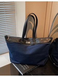 Large denim tote bag with black leather straps and silver zipper on a design book