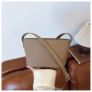 Close-up of khaki pebbled leather bucket bag with adjustable strap in minimalist setting