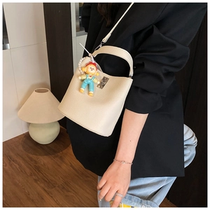 Chic cream-colored small bucket crossbody bag with a colorful doll keychain detail