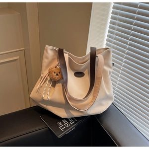 Gros plan du sac cabas en toile beige avec anses en cuir marron et breloque ours peluche