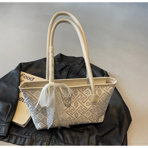 Detail of cream bucket bag featuring geometric embroidery and a lace bow on leather jacket