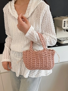 Pink hand-woven bucket bag with drawstring closure held by a model in a modern interior