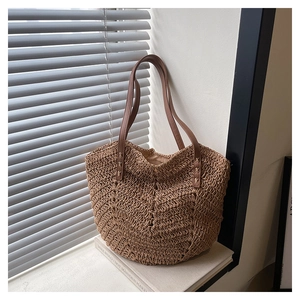 Detail of woven straw tote bag with brown leather handles and wavy textured pattern