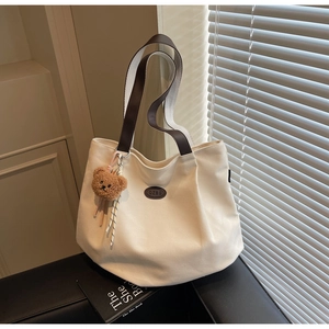 Gros plan d'un sac cabas en toile beige avec anses en cuir brun et breloque ours