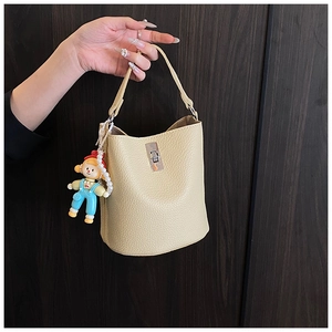 Detail of beige litchi grain bucket bag with metal twist lock and cartoon pearl charm