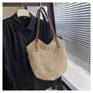 Detail of woven straw tote bag with brown leather straps and cross-stitch craft