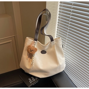 Détail d'un grand sac cabas en toile avec poignées en cuir marron et un charme d'ours