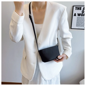 Detail shot of a black litchi pattern crossbody bucket bag on a white suit outfit