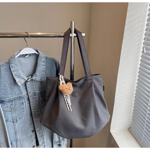 Détail du sac cabas en toile gris avec anses en cuir et petit pendentif ours en peluche