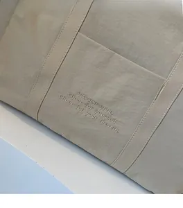 Detailed macro view of beige nylon tote bag fabric texture with white embroidery details