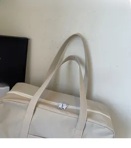 Detail of the reinforced straps and dual white zippers on a cream travel tote bag