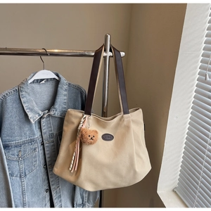 Vue détaillée d'un sac cabas en toile beige avec anses en cuir marron et pendentif ours