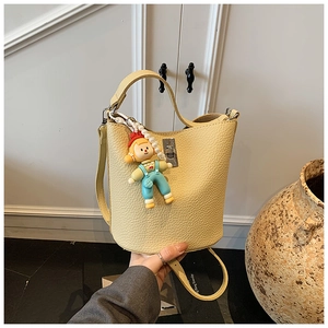 Detail of light yellow bucket bag featuring lychee grain texture and a cute doll charm