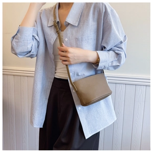 Close-up of tan lychee grain leather crossbody bag worn with a striped shirt