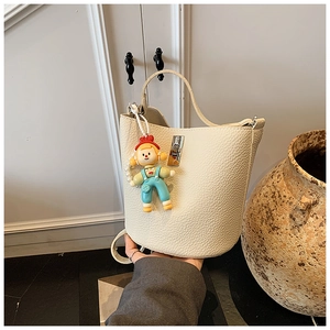 Detail of off-white lychee pattern bucket bag with cute cartoon doll and pearl charm