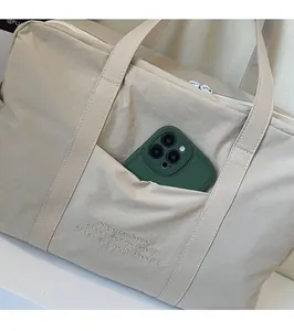 Detail of front pocket on nylon tote bag with embroidery holding a green smartphone
