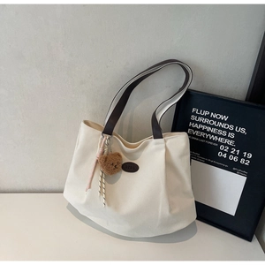 Détail d'un sac cabas en toile beige avec lanières en cuir brun et pendentif ours