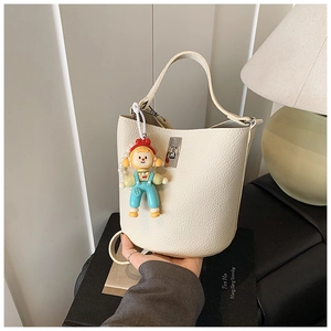 Close-up of beige lychee leather bucket bag with silver lock and cartoon doll charm