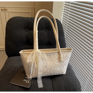 Detail view of a beige tote bag with floral patterns and lace ribbon on a blue chair