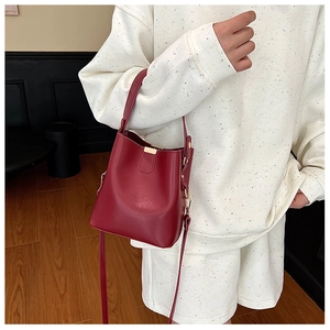 Detail of red matte bucket bag featuring golden buckle and adjustable shoulder strap