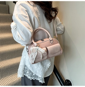 Close-up of pink woven handbag featuring lace bow, pearl pendant and silver metal hardware