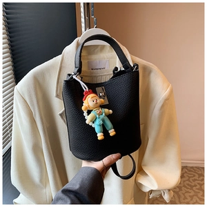 Detail of black lychee leather bucket bag with silver lock and a cute doll pendant