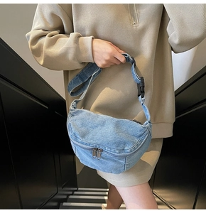 Close-up of light blue denim crescent crossbody bag with adjustable strap and buckle
