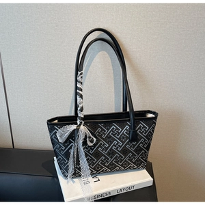 Detail of black tote bag with geometric patterns, lace ribbon bow and leather handles