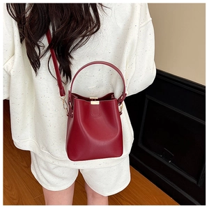 Detail of dark red bucket bag showing golden hardware and smooth leather on model