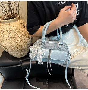 Detail of light blue Boston bag featuring woven texture and lace pearl charm pendant