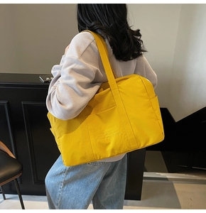 Detail view of large yellow nylon tote bag with multiple outer pockets on model