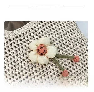 Dettaglio della borsa tote in rete intrecciata con fiore in tessuto 3D e steli verdi